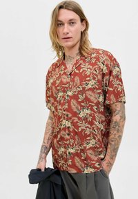 Camisa de manga corta de color óxido con un cuello tipo solapa, que presenta un patrón de plantas tropicales y flores, hecha de una tela ligera.