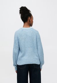 Camisola de malha azul-claro com corte folgado, textura canelada e ombros caídos, combinada com calças de ganga escuras.