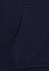 Tissu de sweat-shirt bleu marine avec une texture côtelée et une poche kangourou. Présente des coutures robustes et des bords lisses, offrant une apparence uniforme.