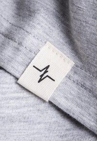 Gray fabric with a soft texture. A label in white cloth featuring a black heartbeat line design is stitched at the edge.