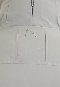 Ljusgrå plagg med dragkedjestängning och subtil sömnad. Ovanlig detalj inkluderar silverbroderad accent på baksidan.