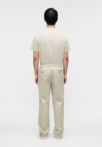 Ανοιχτό μπεζ κοντομάνικο πουκάμισο με διακριτό υφασμάτινο μοτίβο, συνδυασμένο με φαρδιά, ανοιχτό γκρι παντελόνια με σχοινί στη μέση και πίσω τσέπες.