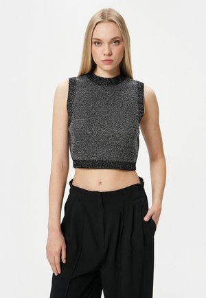 Top corto senza maniche in maglia nera e grigia metallizzata, con un motivo testurizzato e colletto a coste, abbinato a pantaloni neri larghi.