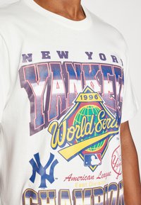 Balta medvilninė marškinėliai su dideliu, spalvingu „New York Yankees Pasaulio Čempionatas 1996“ grafiniu paveikslu, kuriame pavaizduoti beisbolo kamuolys ir pasaulio žemėlapio ikonėlės.
