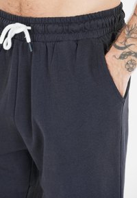 Tummansinisiä puuvillajoggers-housuja, joissa on joustava vyötärö, säädettävä naru ja sivutaskut. Pehmeä kuitu, rento istuvuus.