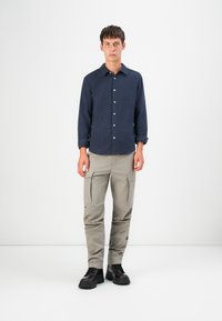 Marineblauwe lange mouwen shirt met knopen aan de voorkant, gecombineerd met lichtbeige cargobroek met zijzakken, en zwarte veterschoenen.