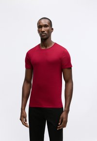 T-shirt rossa in cotone con scollatura tonda e maniche corte, abbinata a un pantalone nero semplice. Tessuto morbido, design aderente.
