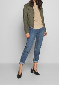 Olivengrøn denimjakke, ribbet beige sweater, blå opsmøgede jeans og sorte højhælede sko. Glatte teksturer og afslappet pasform.