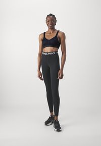 Svart sports-bh med meshinformasjon, kombinert med høyhårede svarte leggings med en hvit "Nike Pro" midjebånd og svarte treningssko.