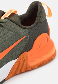 Urheilusandaalit, joissa on vihreä verkkoyläosa, oranssit yksityiskohdat, teksturoitu ulkopohja ja erottuva kantakappale. Kirkas oranssi veto-nappula mukana.