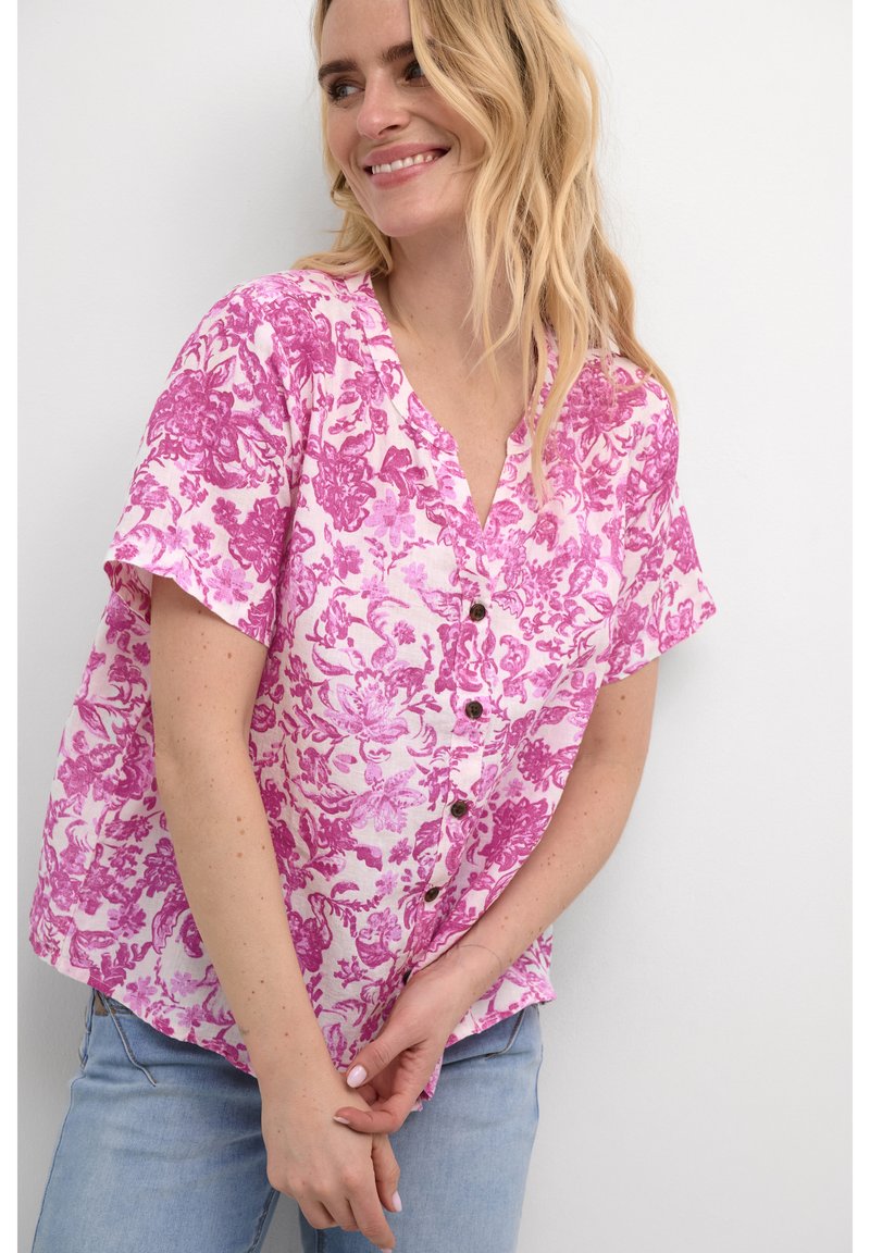 Camicia rosa a maniche corte con scollatura a V e bottoni, realizzata in tessuto leggero. Presenta una vestibilità ampia e un motivo testurizzato.