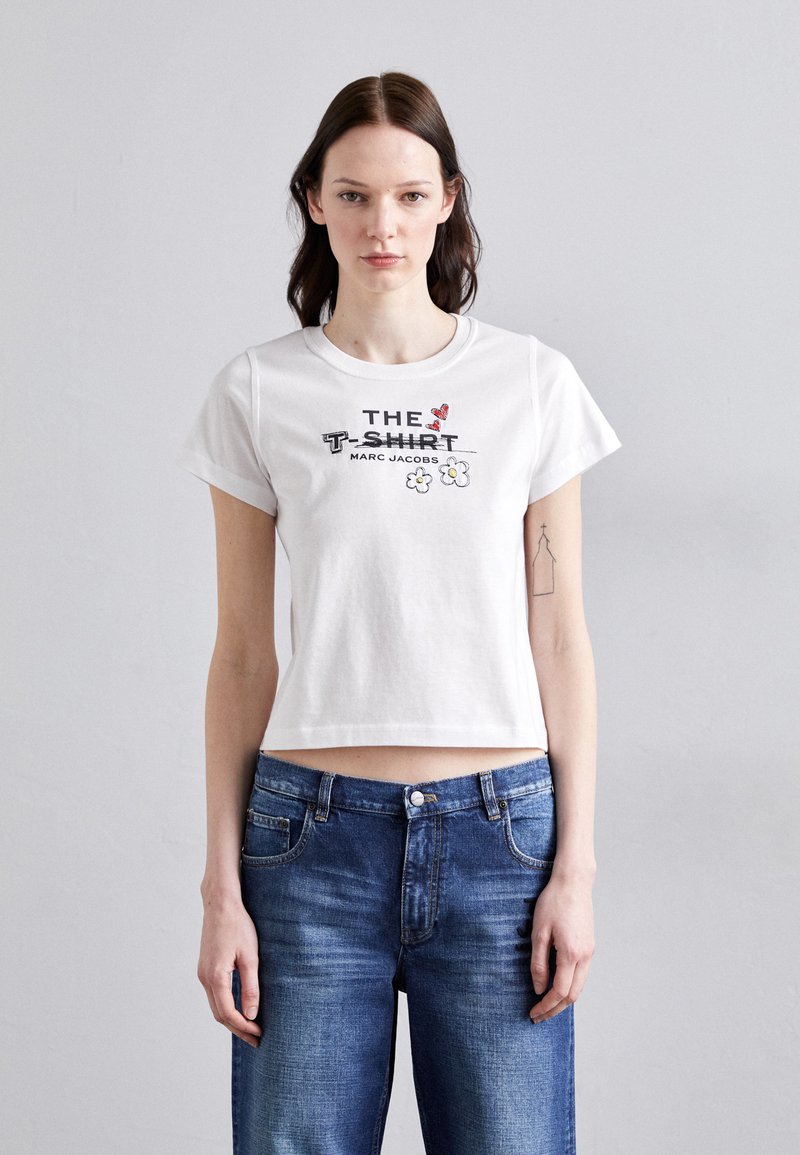 Hvit bomullcroppet t-skjorte med grafisk tekst og blomsterdesign, korte ermer og rund halslinning, kombinert med blå denimjeans.