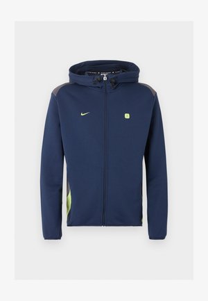 Marineblå Nike jakke med lynlås hele vejen og hætte, lysegrønt logo og detaljer samt snore i hætten mod ensfarvet baggrund.