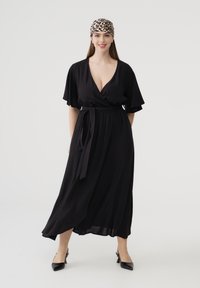 Abito nero avvolgente con maniche a volant corte e vita con cintura, caratterizzato da un profondo scollo a V e una silhouette fluida. Indossato con una fascia per capelli a stampa leopardata.