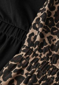 Tissu noir d'un côté et beige avec imprimé léopard noir de l'autre, avec des fronces élastiques à la taille pour plus de flexibilité.