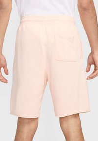 Calções de algodão pessegueiro com cintura elástica, bolso traseiro e design simples. Apresentam uma bainha crua e um discreto detalhe do logo de um lado.