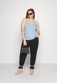 Camisola azul clara com alças finas, combinada com calças pretas largas e saltos bloco rosa claro. A segurar uma pequena mala preta.