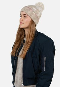 Navy bomber jacket with a zip closure and ribbed cuffs, paired with a beige knitted beanie featuring a pom-pom and colorful patterns.