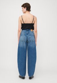 Hochgeschnittene, weit geschnittene blaue Jeans aus Denim mit leichter Ausbleichung, ausgestattet mit einem braunen Lederpatch auf der Rückseite und zwei Gesäßtaschen.