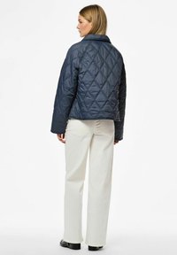 Tamsiai mėlynas siuvinėtas švarkas su apykakle, pasižymintis geometriniu deimantų raštu ir ilgomis rankovėmis, derinamas su kreminiais plačiakulkšniais keliais.