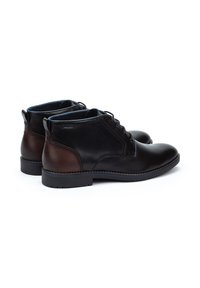 Las botas de cuero negras hasta el tobillo cuentan con un acento de cuero marrón en el talón, con un diseño de cordones y una suela de goma resistente. El interior es de color azul.