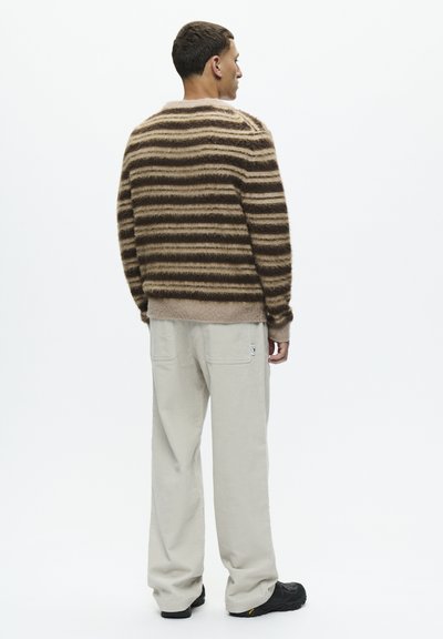 Pull marron rayé avec une texture duveteuse, associé à un pantalon large beige clair. Présente une coupe décontractée et un design simple.