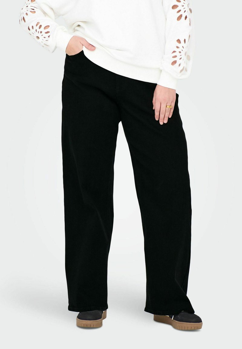 Pantalons noirs à jambes larges en matière douce, dotés d'une taille haute et d'une coupe décontractée. Associés à un sweat-shirt blanc avec des détails découpés.