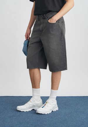 Sivé rifľové šortky s voľným strihom, štandardnými vreckami a pútkami na opasok. Kombinované s bielymi športovými topánkami a textúrovanými bielymi ponožkami.