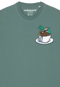 Grünes Baumwoll-T-Shirt mit einem Grafikdesign eines Bechers, der Landschaftselemente zeigt: Palmenbaum, Surfbrett und Berge, umrandet in Schwarz.