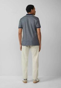 Graues Poloshirt mit navyfarbenem Kragen und Ärmelbündchen, kombiniert mit hellcremefarbenen Hosen. Das Shirt hat einen strukturierten Stoff und kurze Ärmel.