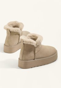 Beiga mockaskängor med en fluffig tanfärgad pälsinredning, stabil plattformssula och sydda detaljer runt kanterna.