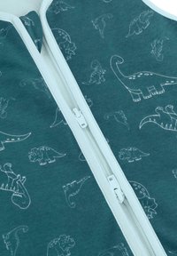 Weißer Reißverschluss auf teal-farbenem Stoff mit weißen Dinosaurierumrissen, einschließlich Mustern von Triceratops, Brachiosaurus und Stegosaurus.