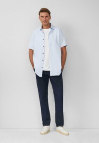 Camicia azzurra chiara a maniche corte con bottoni scuri, abbinata a pantaloni blu navy e sneakers bianche. Design semplice e pulito con una vestibilità rilassata.
