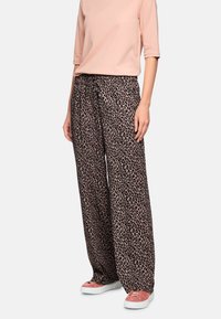 Leopard-print wide-leg trousers made of soft fabric, featuring a drawstring waistband and relaxed fit, paired with light pink top and pink sneakers.
