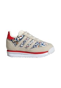 Beige sneakers with floral pattern, red accents, three white stripes, and white rubber sole. Suede and textile materials used in design.