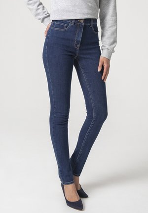 Jeans ajustados de denim de color azul oscuro, que cuentan con bolsillos frontales, cierre de botón y un diseño ceñido con una textura suave.
