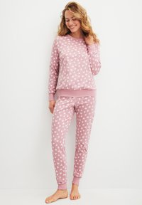 Roze pyjama set met een lange mouwen top met kleine witte hartpatronen en bijpassende broeken met vergelijkbare ontwerpen. Zacht katoenmateriaal.