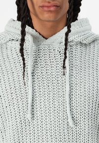 Sudadera de punto azul claro con una textura de tejido abierto, que cuenta con un capucho ajustable y un diseño de corte suelto.