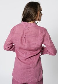 Roze linnen overhemd met een kraag, lange mouwen en een schouderpas detail; heeft een relaxed fit en zijsplitten aan de zoom.