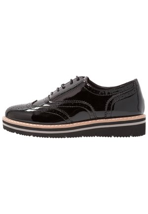 Chaussures en cuir verni noir à lacets avec des détails en brogue, un bout arrondi et une semelle texturée en noir et blanc superposée.