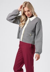 Kraftigt mönstrad svartvit jacka med vit krage, knappstängning och stora knappar, i kombination med vinröda byxor.