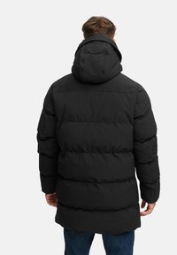 Abrigo acolchado negro con capucha, con costuras horizontales y un ajuste holgado. La tela parece suave y ligera.