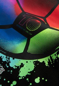 Nahaufnahme eines farbenfrohen Fußballpaneels mit dem Text "10. ANN Nations Cup" und einem holografischen Globus-Muster auf schwarzem Hintergrund.