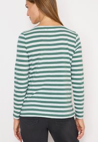 Maglietta a maniche lunghe con un motivo a righe orizzontali verde e bianco, scollo rotondo e una texture di tessuto morbido. Indossata con jeans neri.