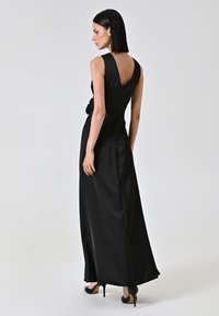 Schwarzes Satin-Abendkleid mit tiefem V-Ausschnitt im Rücken, ärmellosem Design und taillierter Passform, mit einem floralen Akzent an der Seite.