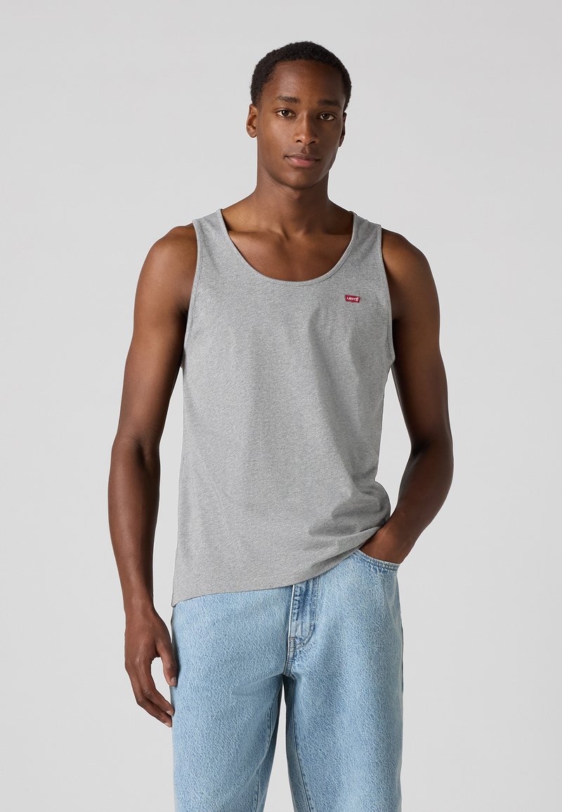 Débardeur en coton gris avec un col rond, arborant un petit logo rouge. Associé à un jean en denim bleu clair, ample.