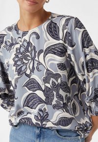 Helles blaues Blusenshirt mit filigranen dunkelblauen Blumenmustern und Blattdesigns, aus glattem Stoff mit rundem Ausschnitt und lockerer Passform.