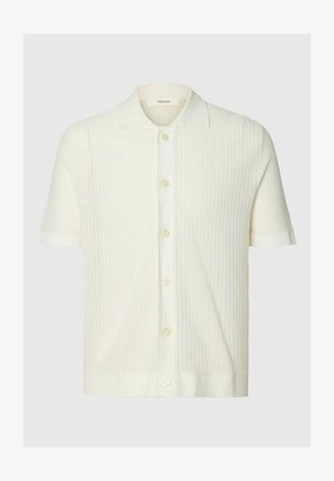 Polo en maille blanche à manches courtes avec patte boutonnée et motif texturé, conçu pour un usage décontracté.