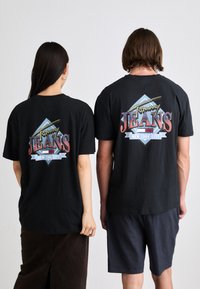 Tricouri negre cu un design grafic colorat pe spate, având textul "Tommy Jeans New York City" și accente geometrice.