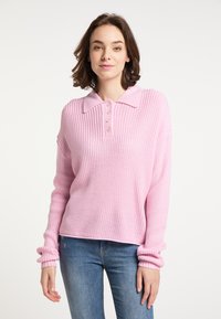 Jasnoróżowy sweter dziany z kołnierzykiem, pięcioma guzikami, długimi rękawami i prążkowanymi mankietami. Noszony z niebieskimi dżinsami.